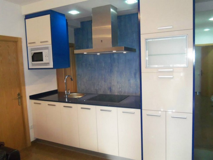 Cocina en forma de isla con muebles en color marfil brillo y costados en azul marino